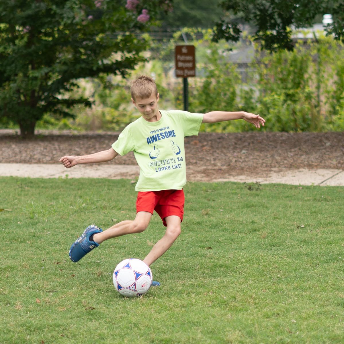 A camper kicking a soccer ball on the grass