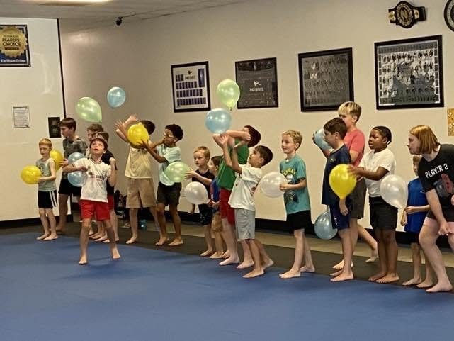 A long line of campers on the blue mats laughing as they keep balloons up in the air