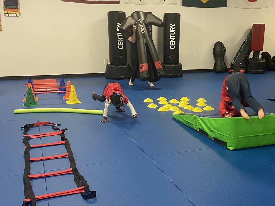 Campers rolling and crawling through an obstacle course with cones, hurdles, an agility ladder and a green tumbling mat