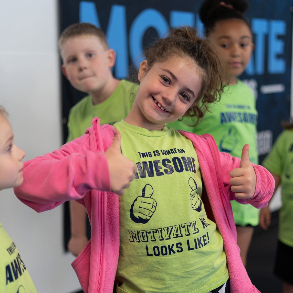 A smiling Motivate student giving two thumbs up in her Motivate shirt